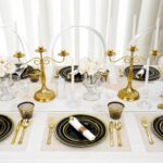realluck 350-piece black plastic dinnerware set with gold rim plates, gold plastic cutlery, black cups, and white napkins.